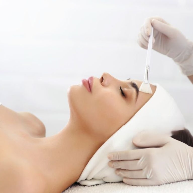 Model in white headband bandage cap lying on couch with closed eyes. Hand of beautician doctor in white glove touching her face with brush. Head and shoulders, healthcare, cosmetology, beauty clinic